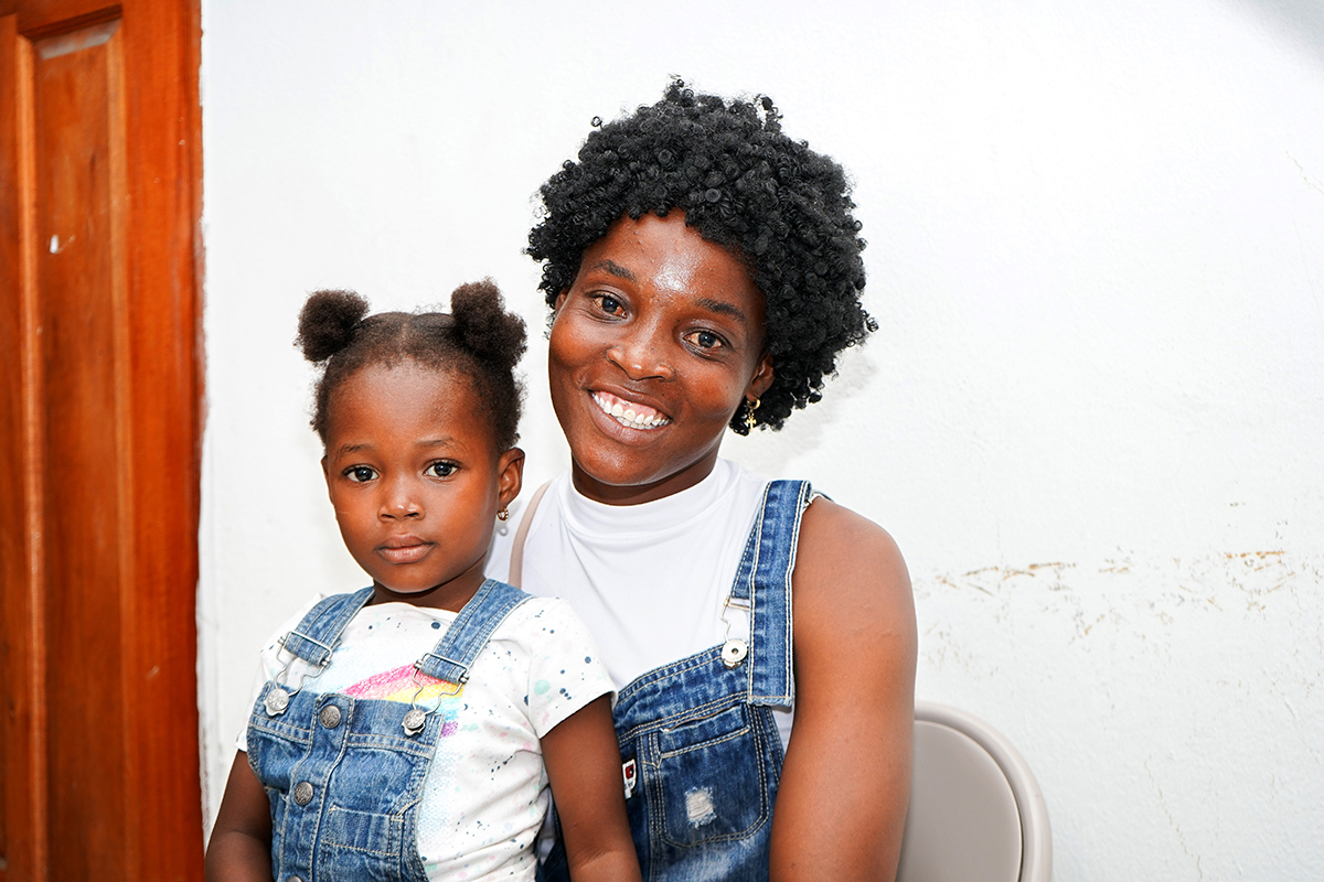 Tatiana sits on her mother Thérèse's lap, both are wearing denim overalls with white shirts underneath