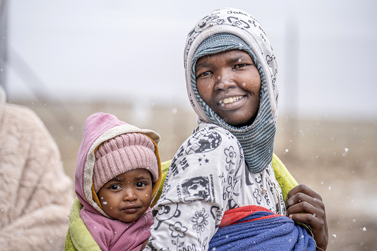 Mother smiles and carries her daughter in snowy Lesotho