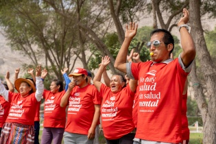 Outside in front of trees, people in red shirts that say "No hay salud sin salud mental" raise their arms in the air, the person closest to the camera has a whistle in their mouth