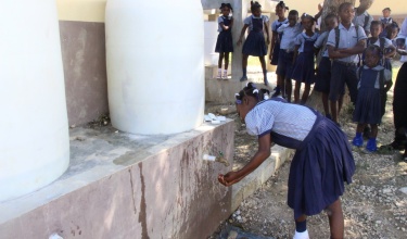 a girl washes her hands with soap and water at a school in Mirebalais, Haiti