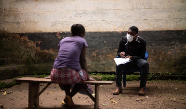 A PIH community health worker wearing a mask speaks to a patient from six feet away.