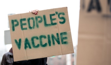 A protester holds a sign that says People's Vaccine