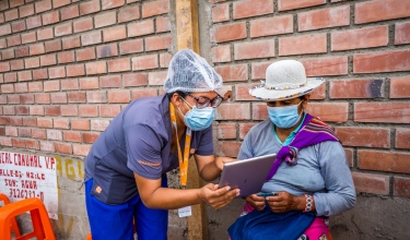 A health worker with Partners In Health helps a patient read health information on a tablet device.