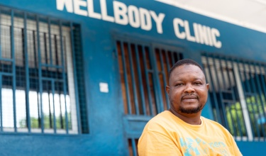Bailor in an orange PIH t-shirt sitting in front of Wellbody Clinic