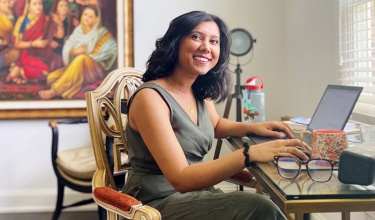 Sita Chadra smiles as she sits in her home office, with her hands on a computer keyboard.