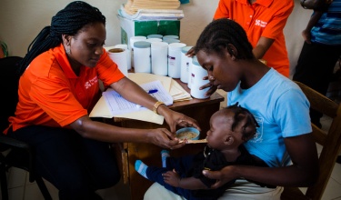 Ms. Esther Mahotiere, a nutrition program coordinator in Haiti, feeds Nourimanba to 8-month-old Wisline Sauvene at the malnutrition clinic in Boucan Carré.