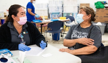 Juana Vidaurri, right, chats with licensed practical nurse Soila Gutierrez before receiving the Covid-19 vaccine at a Healthcare Network of Southwest Florida vaccine inoculation site in Immokalee, FL