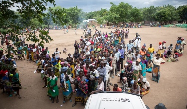 numerous people gathered under a dark sky, lined up behind a van labelled with Partners In Health