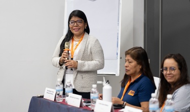 a woman with glasses and a cream blazer stands behind a banquet table with a mic in her hand