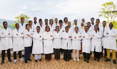 A group of 30 students in white lab coats stand in a group outside on the University of Global Health Equity campus.